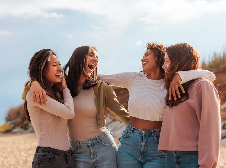Four women with their arms around each other, laughing together outdoors