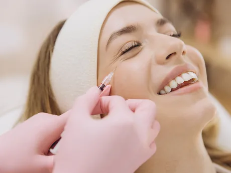 A smiling woman receiving a cosmetic injection near her eye