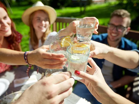 Friends raising glasses of water in a toast at an outdoor table